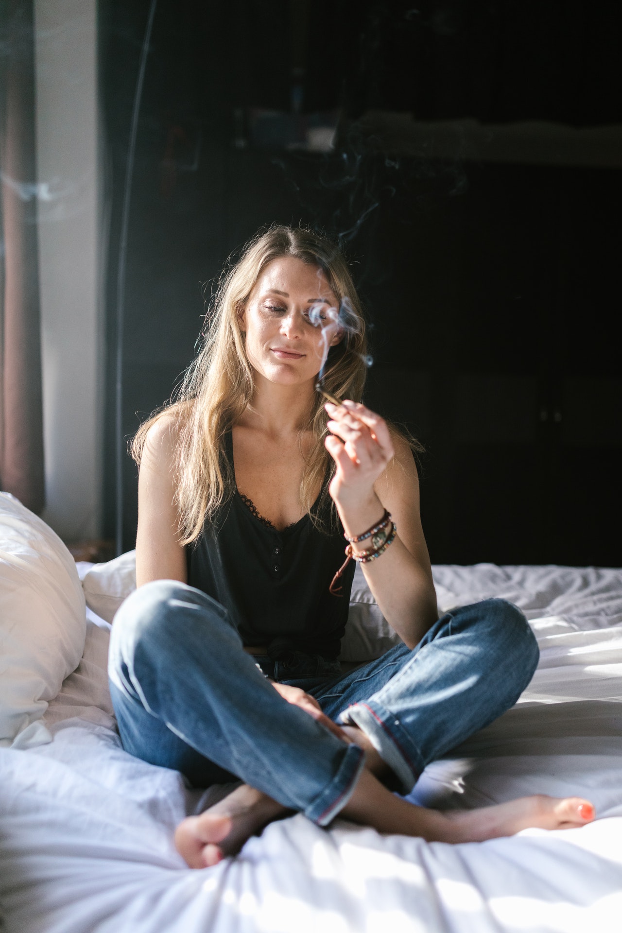 Djevojka sjedi na krevetu i puši marihuanu